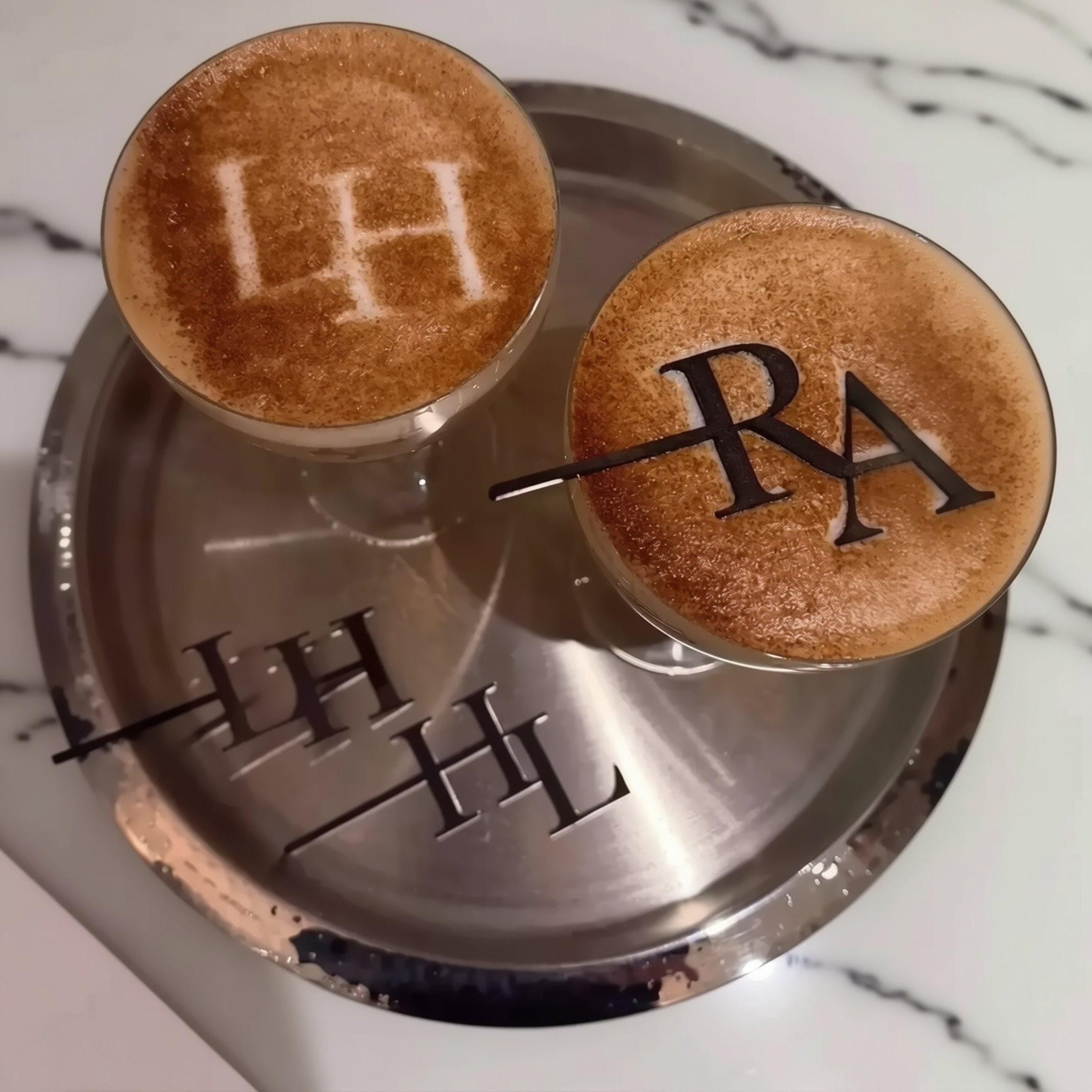 two glasses filled with a beverage, each topped with a decorative design made of cinnamon or sugar.