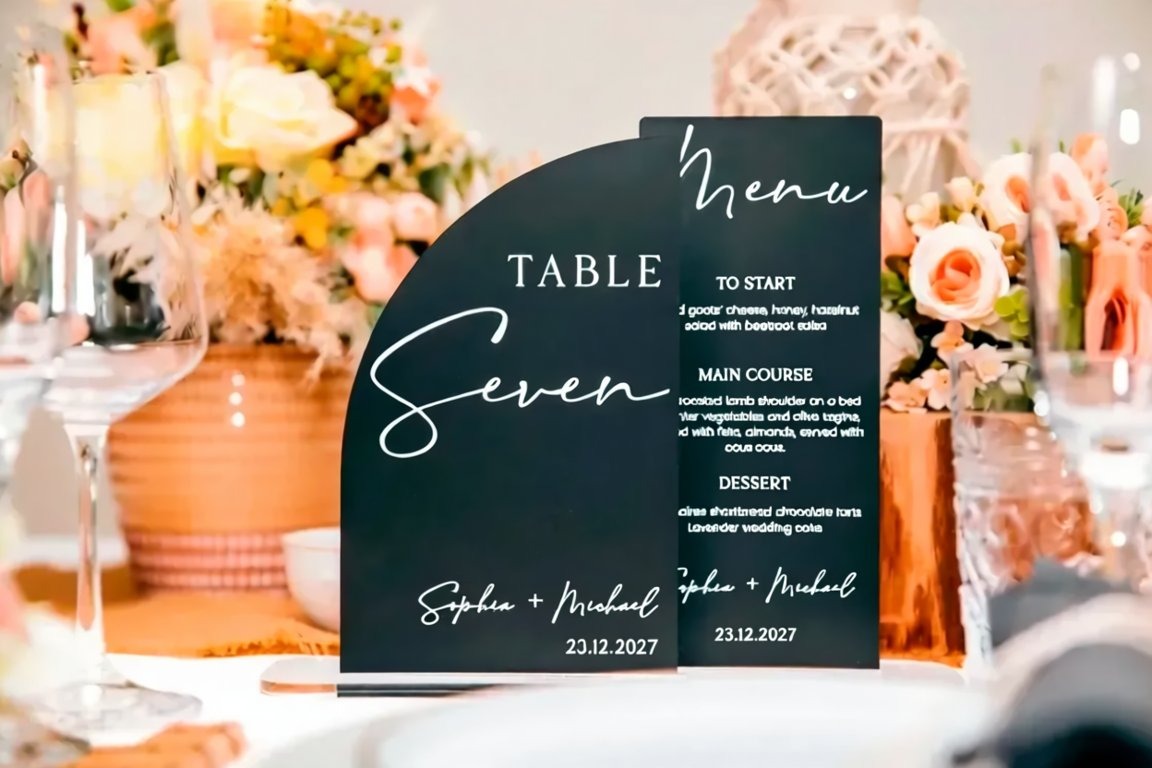 A black and white menu sign for a table called "Seven" with a table setting and floral arrangements in the background.