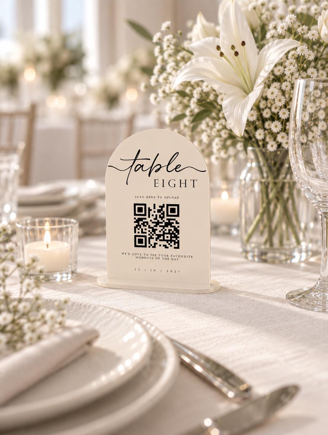 a table setting with a white tablecloth, plates, silverware, and a vase of white flowers. In the foreground, there is a white sign with a QR code and text that reads "Table Eight" and "Scan Here to Pay".