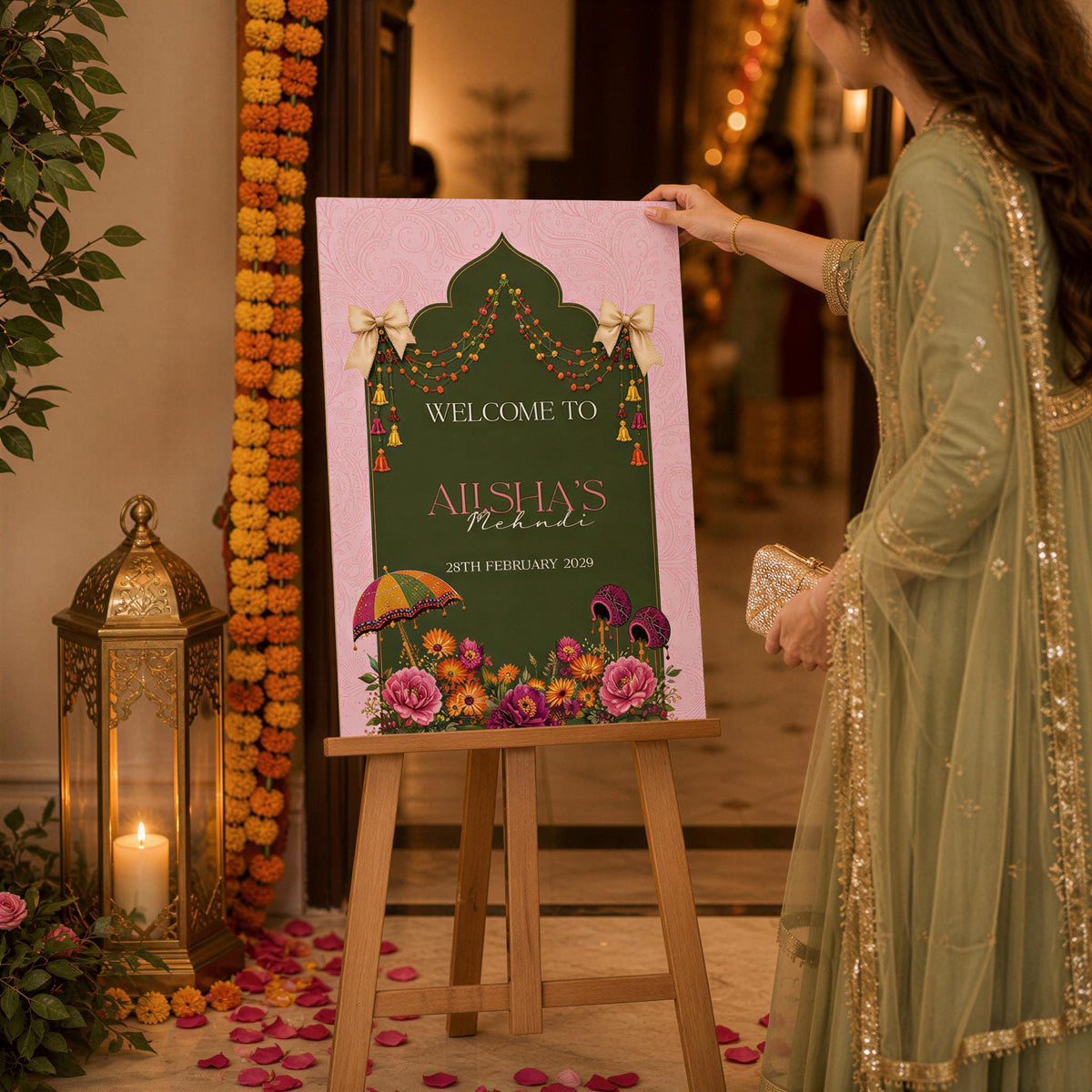 A woman in a green dress is holding a sign that reads "Welcome to Alishu's" in front of a pink and green sign with flowers and a decorative arch.