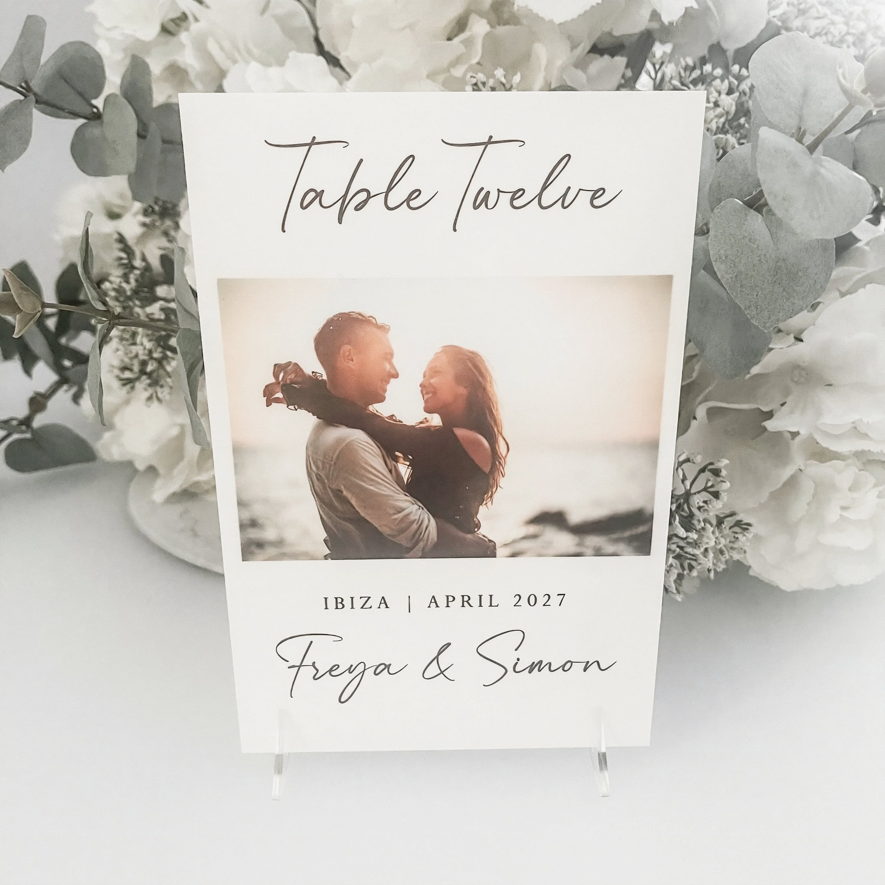 a wedding invitation card with a photo of a couple embracing. The card is titled "Table Twelve" and includes the names "Freya & Simon" and the date "IBIZA | APRIL 2027".