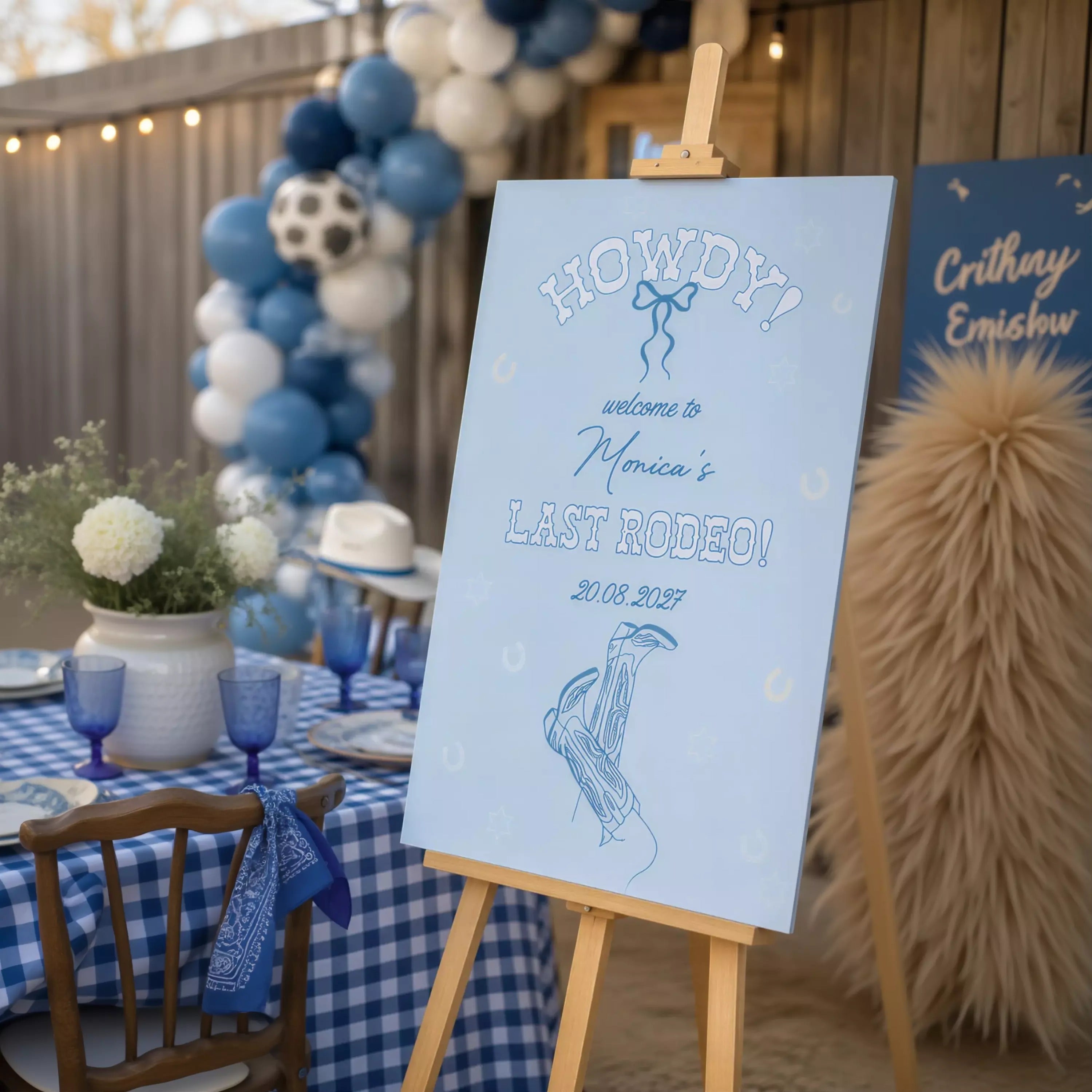a blue and white sign that reads "Howdy! Welcome to Monica's Last Rodeo! 20.08.2037" with a graphic of a pair of cowboy boots. The sign is displayed in front of a table with blue and white checkered tablecloths, and there are balloons and a vase of flowers in the background.