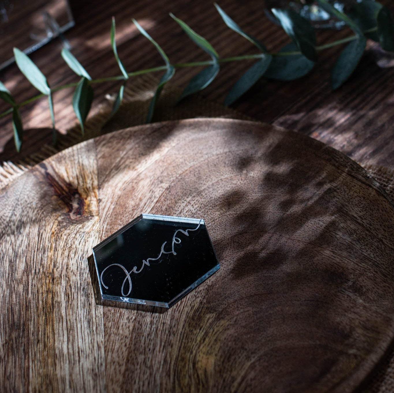 A wooden table with a black hexagonal placemat, a small plant, and a glass of water.