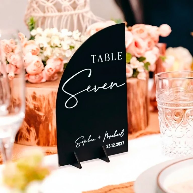 A black table sign displaying "TABLE Seven" is placed on a table with a floral centerpiece.