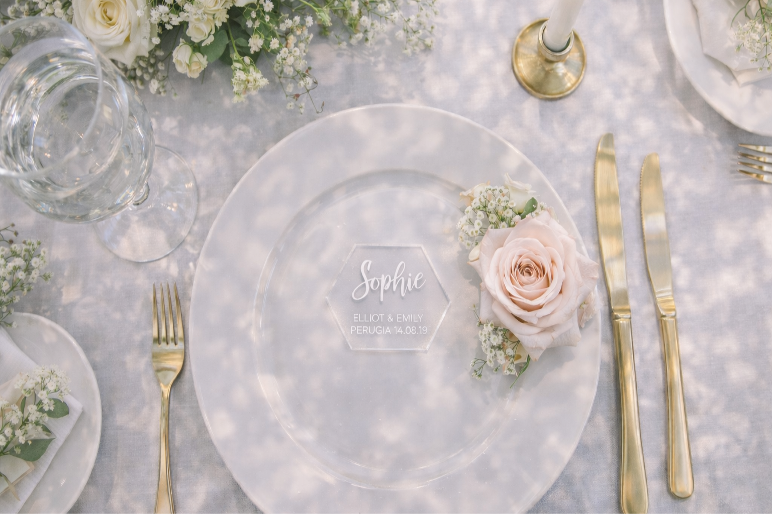 a beautifully set table with a white plate, a rose, and a nameplate. The table is adorned with a floral centerpiece and elegant goldware, creating a sophisticated and inviting atmosphere.
