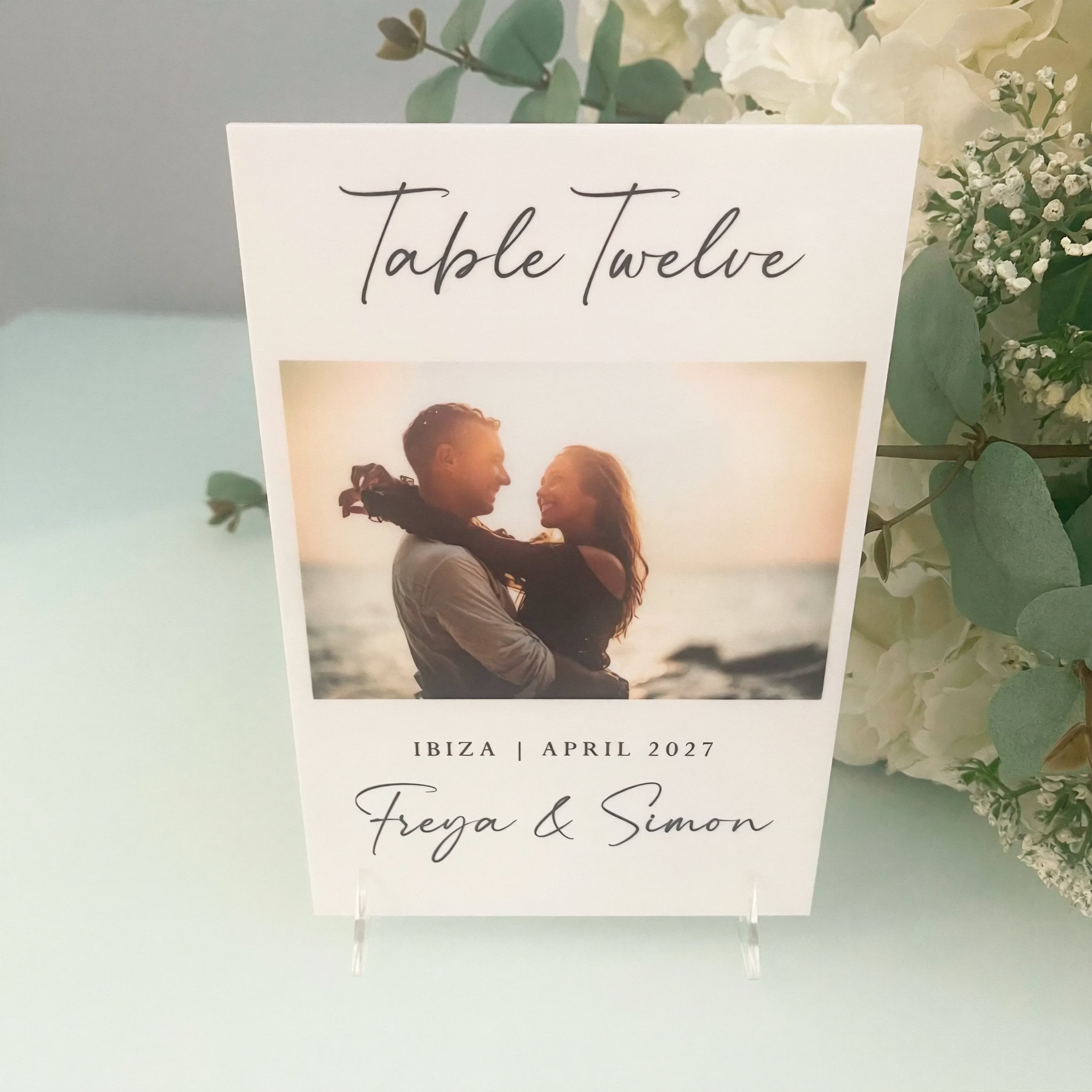 a wedding invitation card with a photo of a couple embracing. The card is titled "Table Twelve" and includes the text "IBIZA | APRIL 2027" and "Freya & Simon".