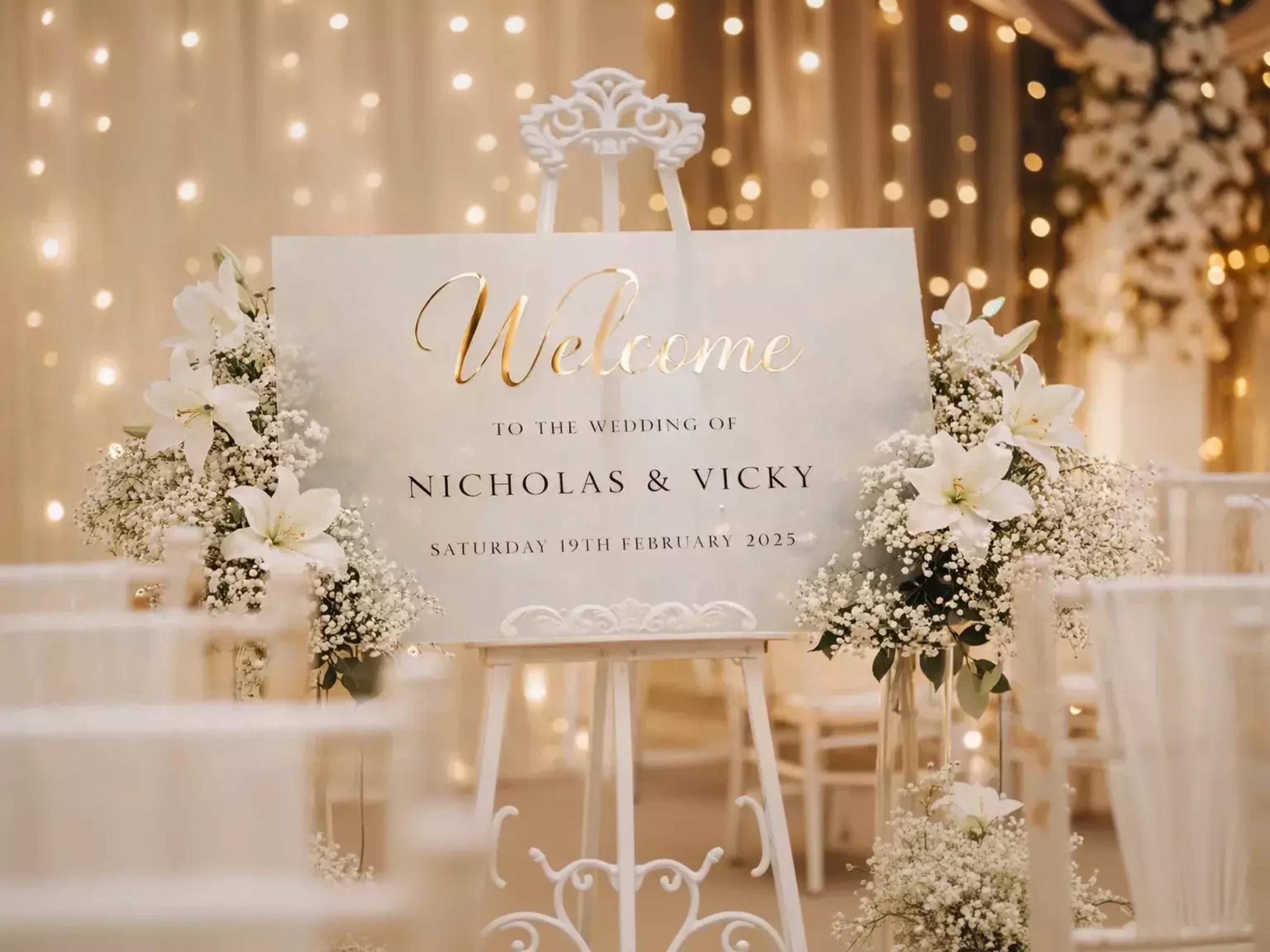 A white sign with gold lettering welcoming guests to the wedding of Nicholas & Vicky on Saturday, 19th February 2015.