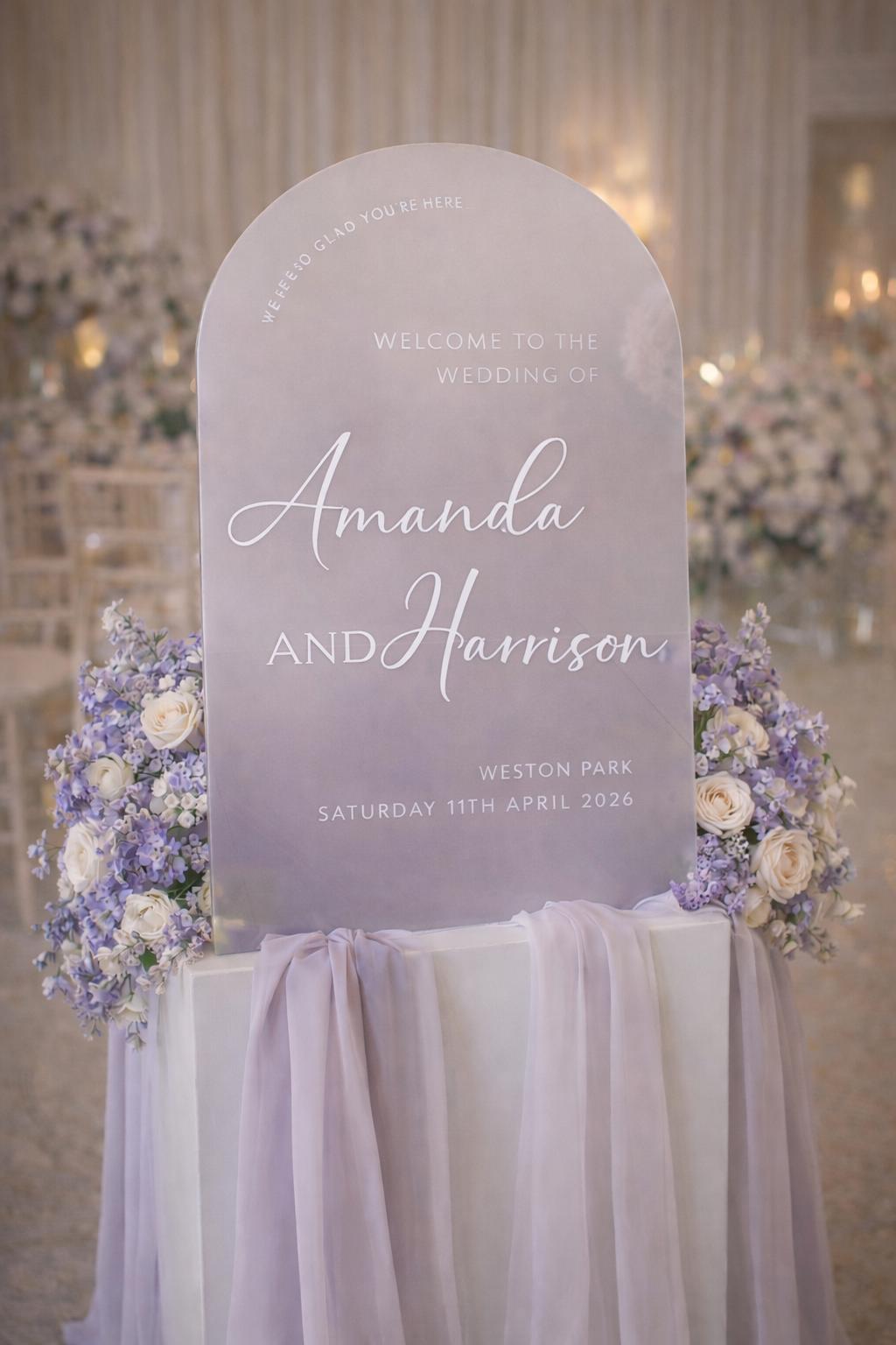 a wedding sign with the names 'Amanda' and 'Harison' written on it, standing in a room decorated with purple flowers.