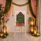 a beautifully decorated room with a pink sign that reads "Welcome to Aishah's 26th February 2019" in the center. The room is adorned with pink and green curtains, lanterns, and flowers, creating a warm and inviting atmosphere.