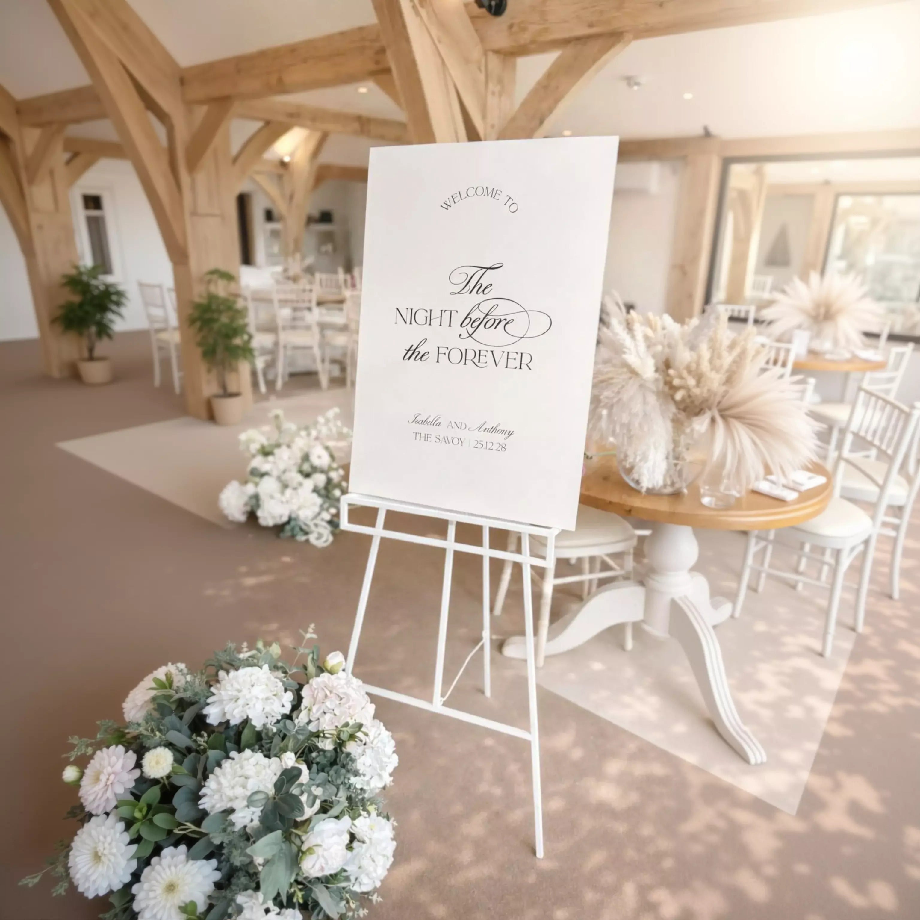 a white sign with black text welcoming guests to an event, placed in a room with a wooden floor and white furniture.
