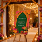 a colorful welcome sign for Priya's Mehendi, which is a traditional Indian wedding ceremony. The sign is displayed in front of a decorated doorway, with a chandelier and flowers visible in the background.