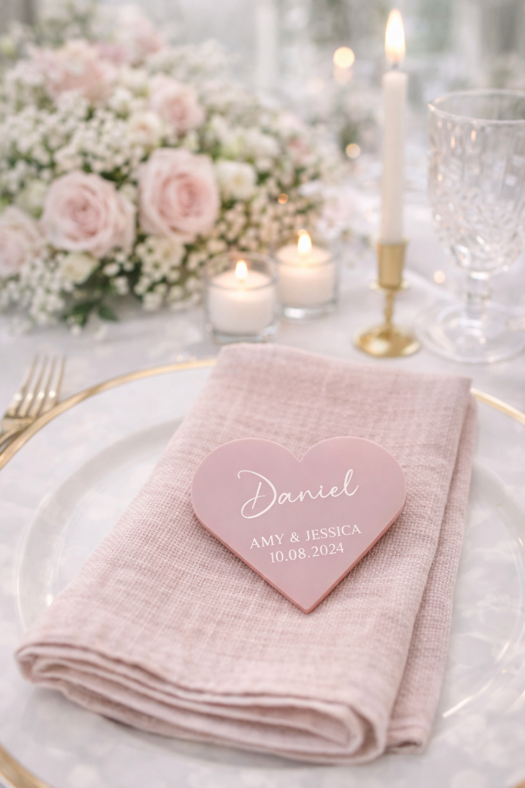 A table setting with a pink napkin, a heart-shaped nameplate, and a floral centerpiece.