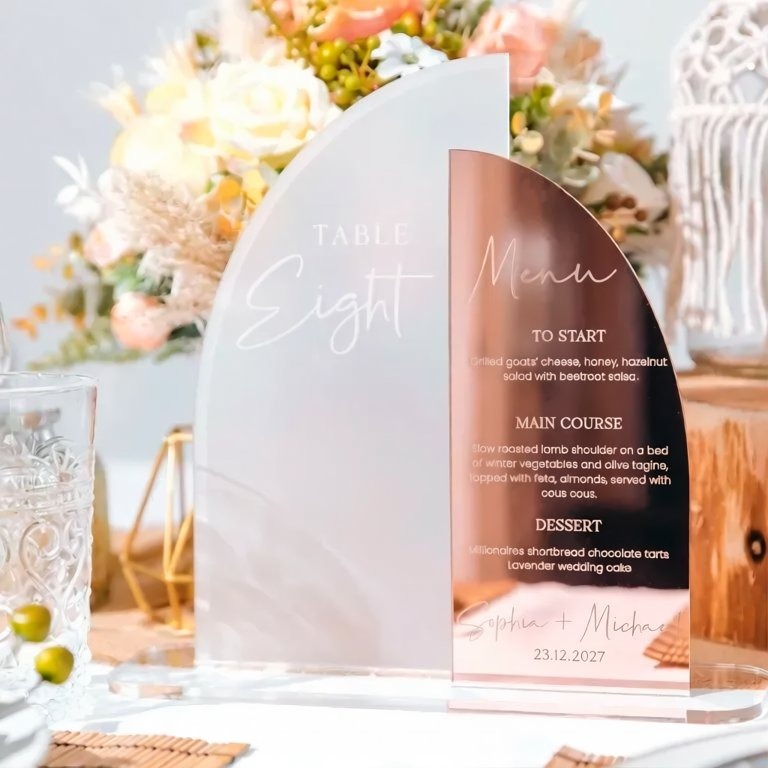 a table setting with a clear glass sign displaying a menu, a glass of water, and a vase of flowers.