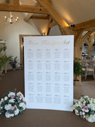 a large seating chart displayed on a white board, with a floral arrangement on either side.