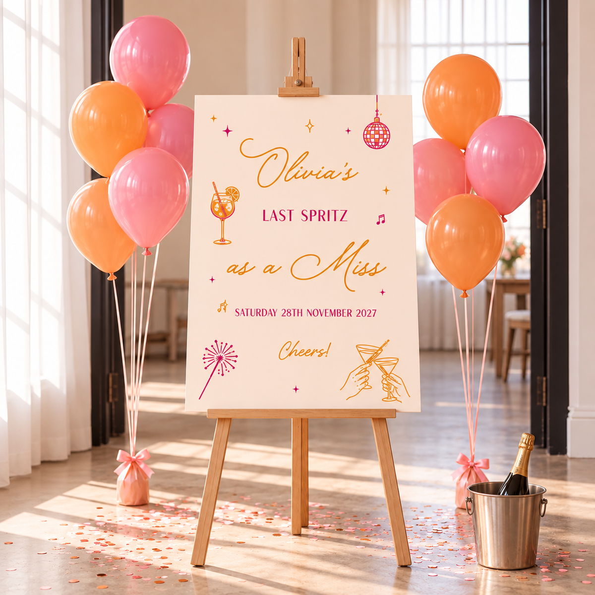 a sign that reads "Olivia's LAST SPIRZ as a Miss" with illustrations of a champagne glass and a champagne bottle. The sign is placed in front of a display of pink and orange balloons, and there is a champagne bucket nearby.