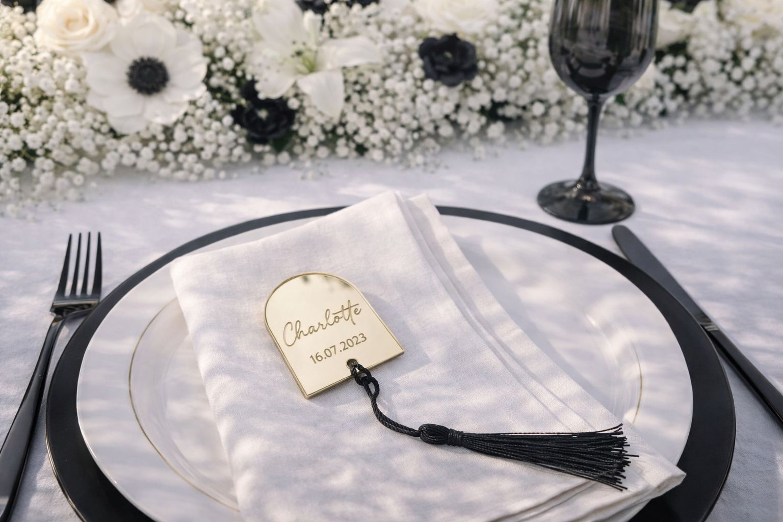 a table setting with a white plate, a napkin, a fork, a knife, and a wine glass. There is also a small gold-colored name tag on the napkin with the name "Charlotte" and the date "16.07.2023".