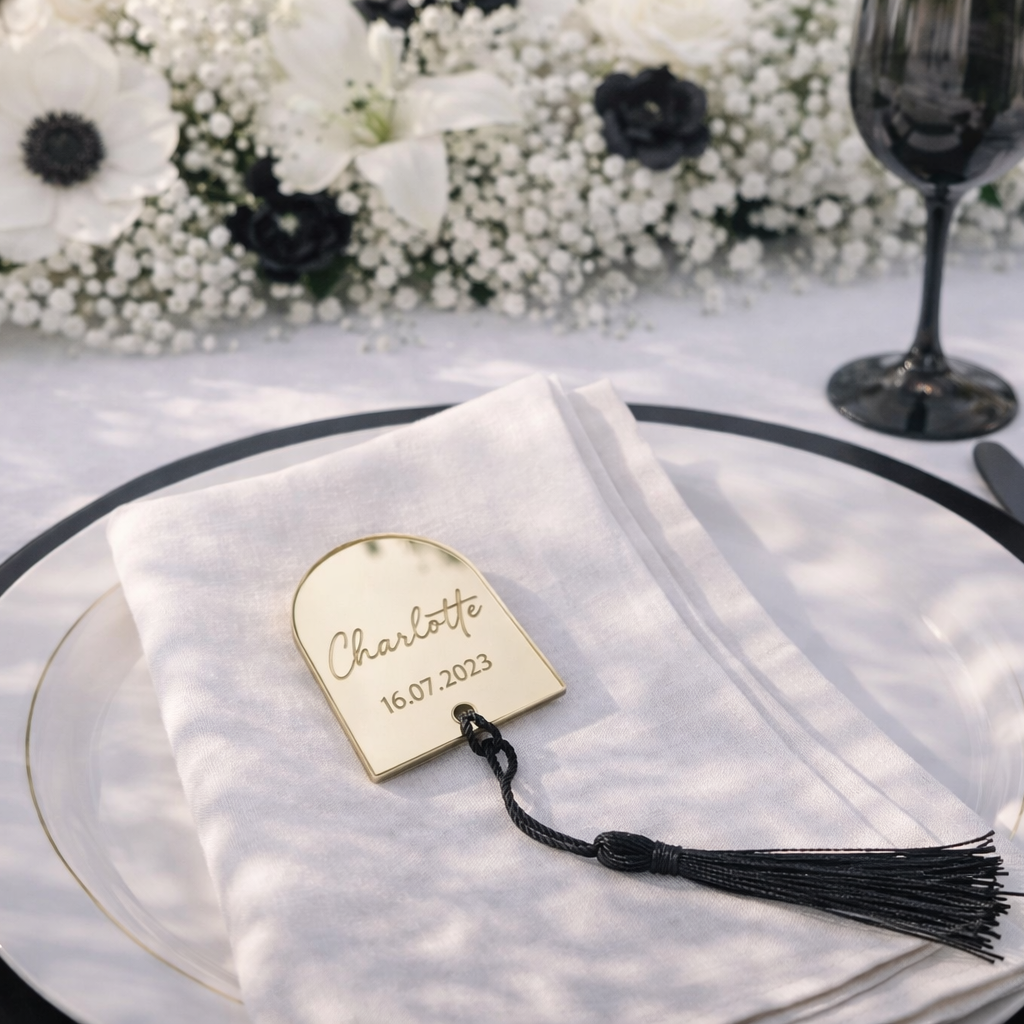 a table setting with a white plate, a napkin, a fork, a knife, and a wine glass. There is also a small gold-colored name tag on the napkin with the name "Charlotte" and the date "16.07.2023".