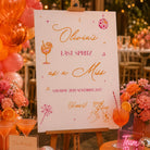 The image is a vibrant and festive party setup, featuring a sign that reads "Olivia's LAST SPRITZ as a MISS" and "Saturday 28th November 2017 Cheers!" The sign is surrounded by various party decorations, including balloons, flowers, and a neon sign that says "Let's Party". The table is adorned with cocktail glasses, oranges, and other party items, creating a lively and celebratory atmosphere.