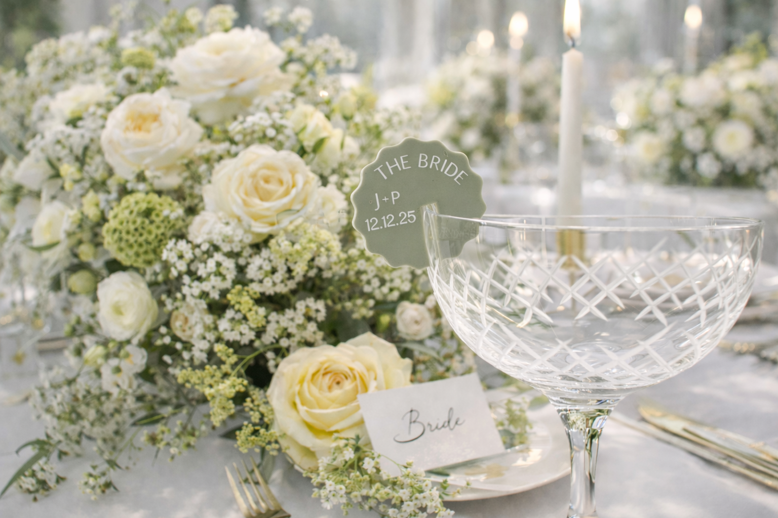 a beautifully decorated wedding reception table with a large floral centerpiece, a glass bowl, and a place card for the bride.