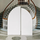 a white archway and a staircase with a wooden railing, set against a backdrop of a tiled floor and a circular pattern.