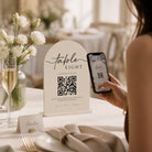 A person is using a smartphone to scan a QR code at a table, with a table setting and flowers in the background.