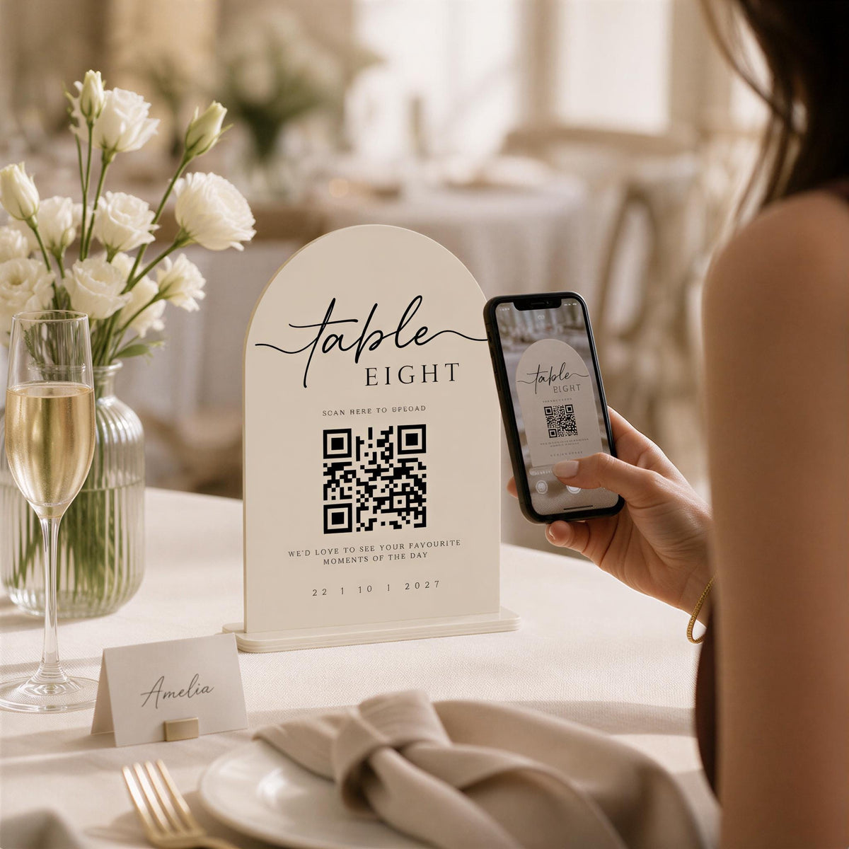 A person is using a smartphone to scan a QR code at a table, with a table setting and flowers in the background.