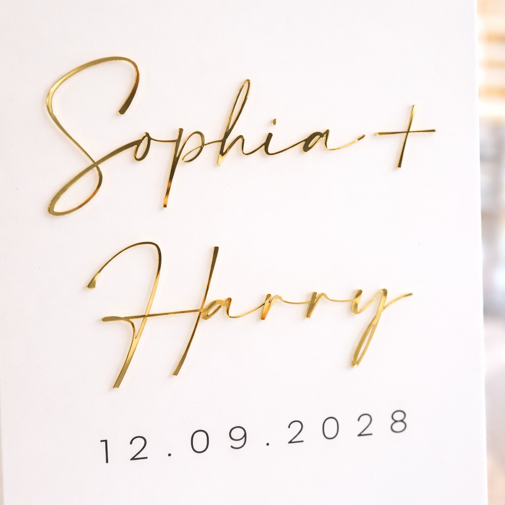 a white surface with gold cursive text that reads "Sophia + Harry" and the date "12.09.2028".