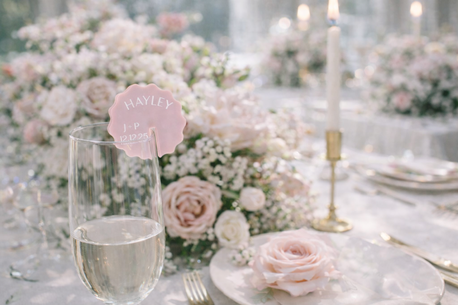 a table setting with a glass of wine, a pink flower, and a candle, all set against a backdrop of beautiful floral arrangements.