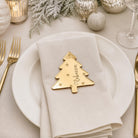 a white plate with a gold-colored tree-shaped place card that says "Rebecca" on it, placed on a table with other tableware and decorations.