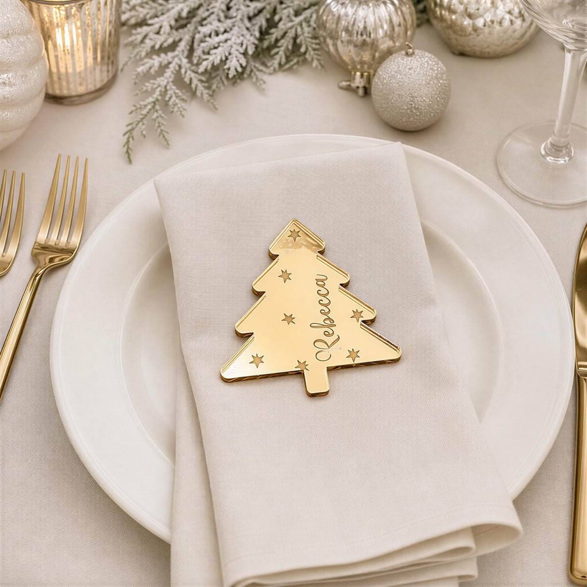 a white plate with a gold-colored tree-shaped place card that says "Rebecca" on it, placed on a table with other tableware and decorations.