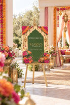 a colorful sign welcoming guests to a special event, with a background of flowers and decorations.