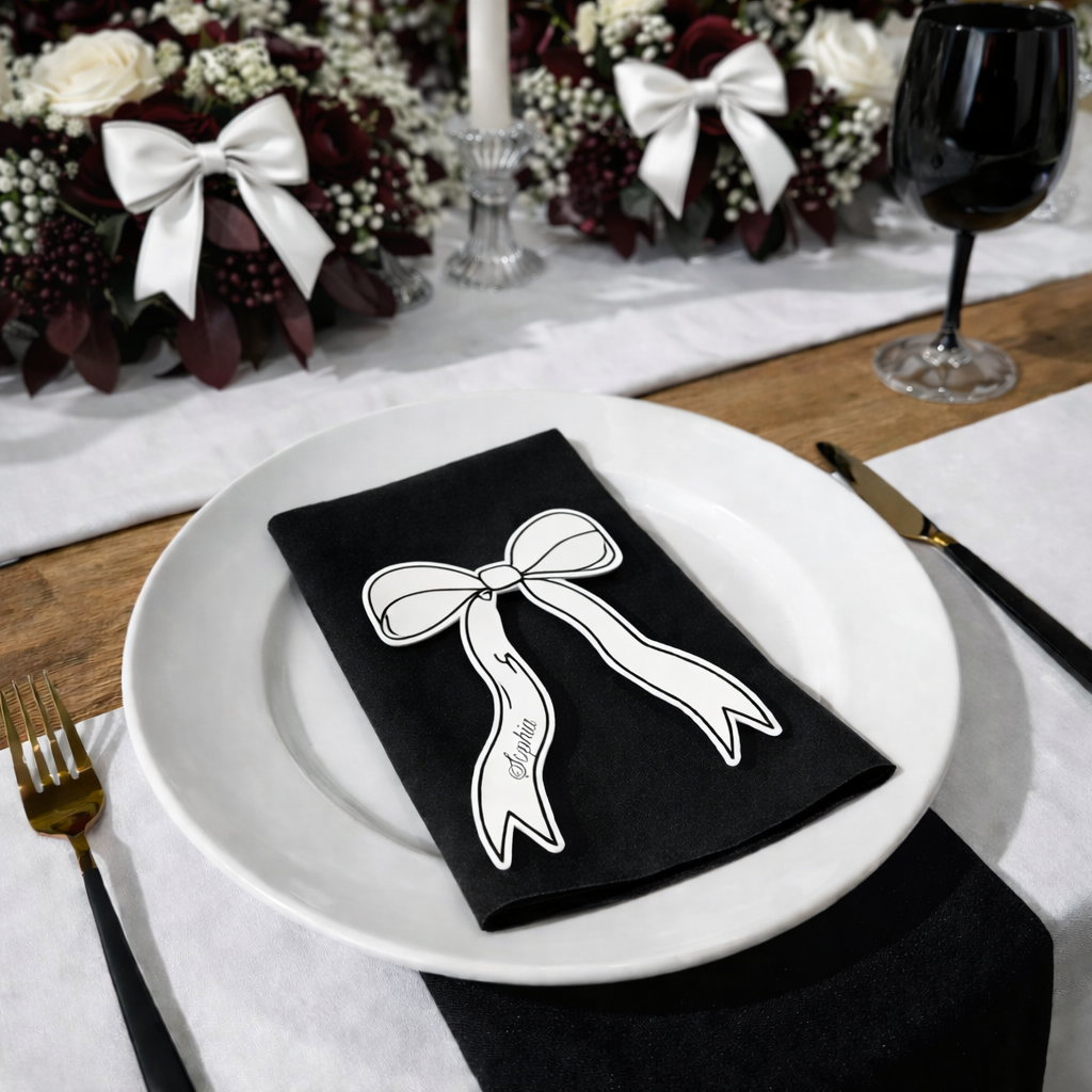 A table setting with a white plate, a black napkin with a bow, a wine glass, and a floral centerpiece.