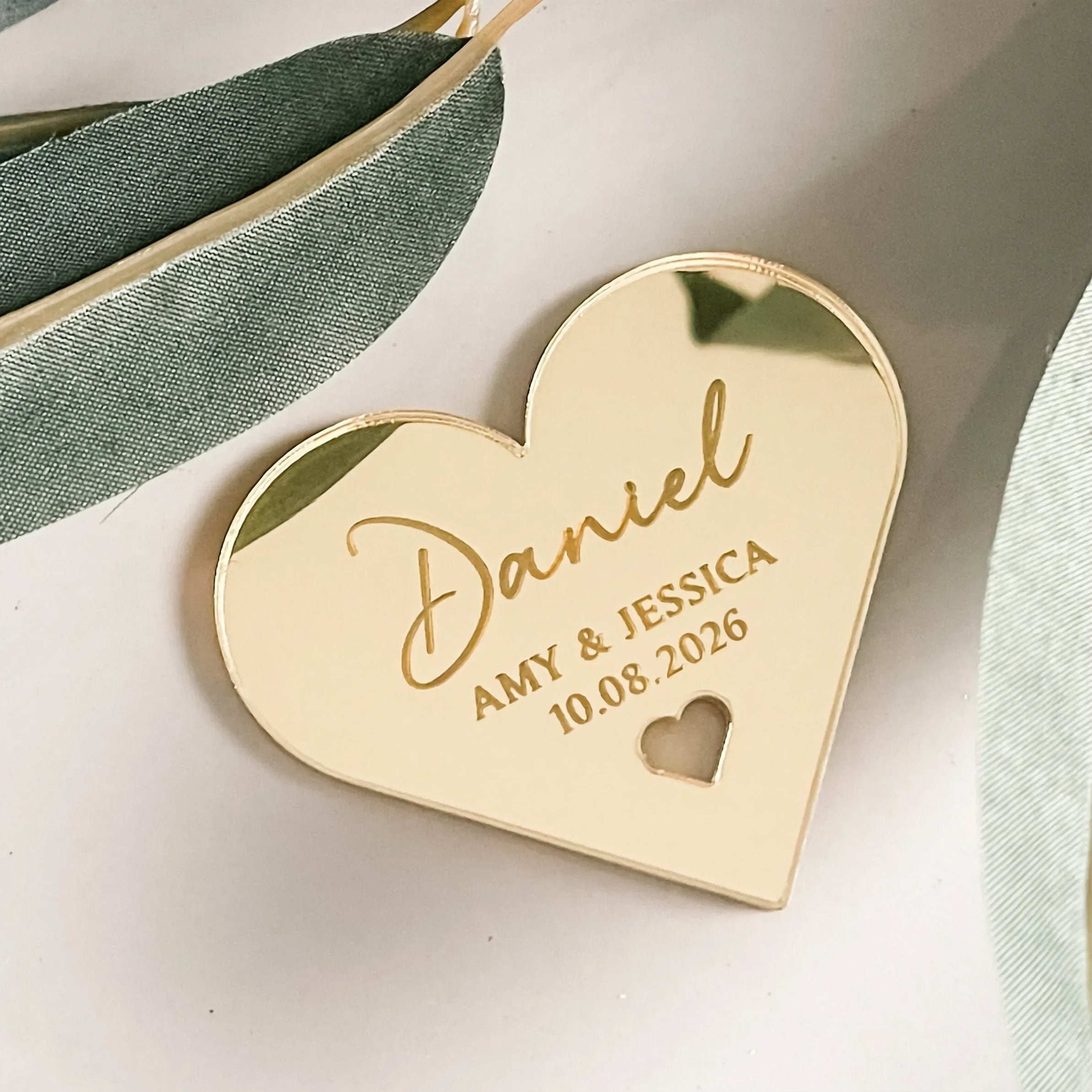 A gold-colored heart-shaped tag with the name "Daniel" and the date "10.08.2026" printed on it.