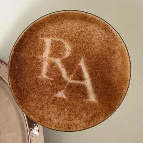 A close-up view of a cup of coffee with a latte art design, featuring a heart shape.