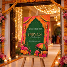 a colorful welcome sign for Priya's Mehndi, which is a traditional Indian wedding ceremony. The sign is displayed in a hallway decorated with flowers and lights, creating a festive atmosphere.