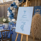 a blue and white sign that reads "Howdy! Welcome to Monica's Last Rodeo! 20.08.2037" with a graphic of a pair of cowboy boots. The sign is displayed in front of a table with blue and white checkered tablecloths, and there are balloons and a vase of flowers in the background.