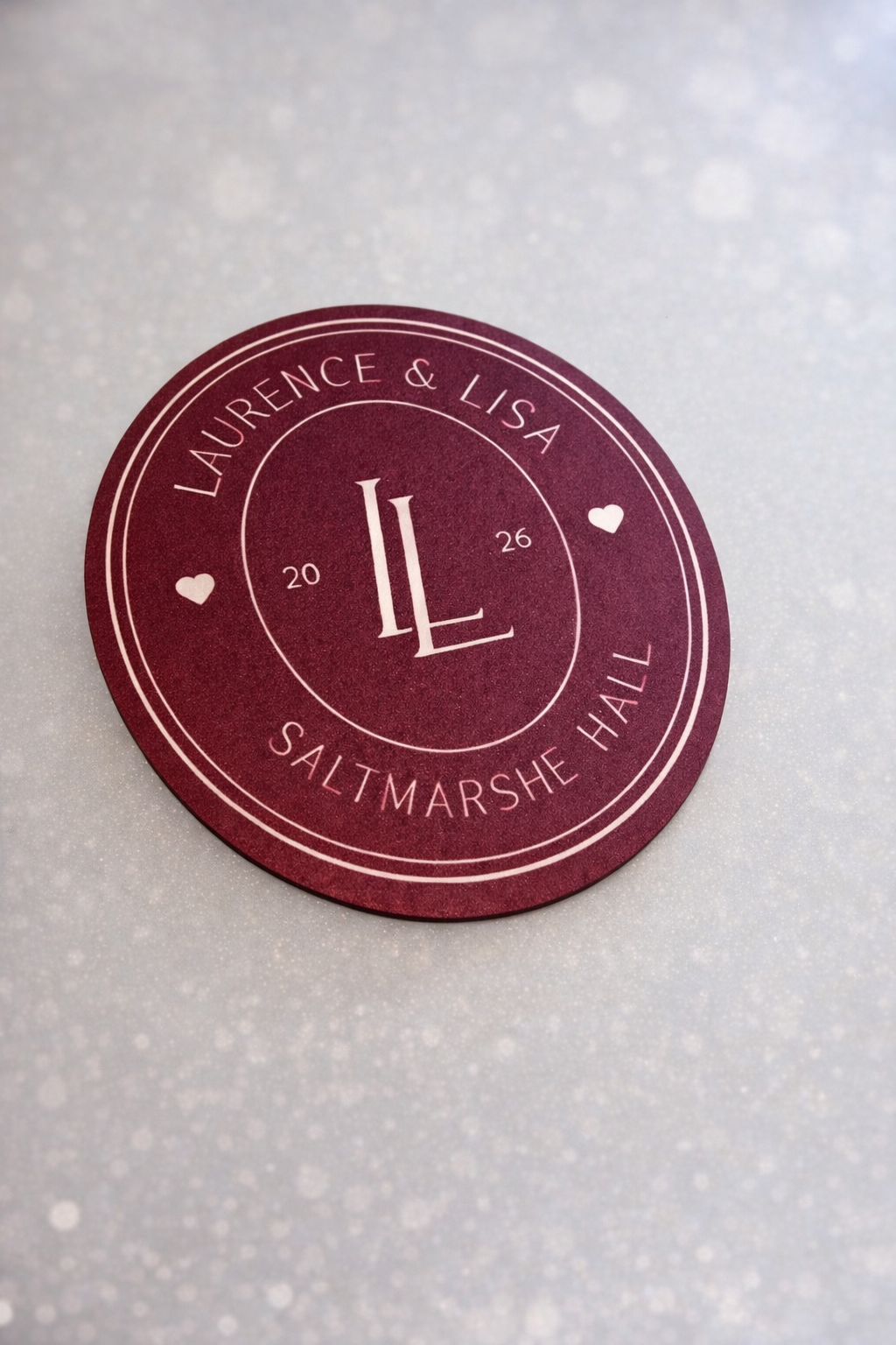A maroon coaster with the text "Laurence & Lisa" and "SALTMARSHE HALL" printed on it.