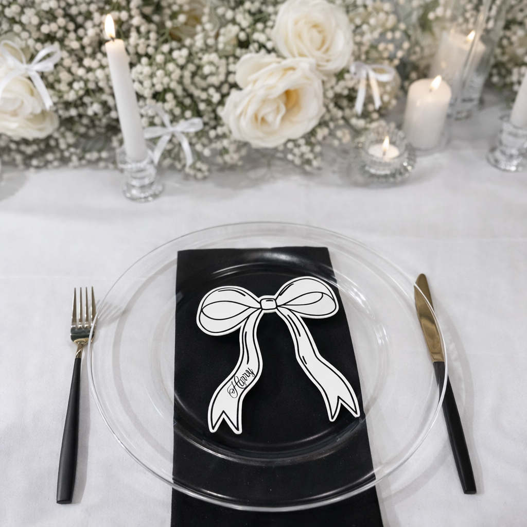 a table setting with a clear glass plate, a black napkin with a bow, a fork, a knife, and a candle. The table is decorated with white flowers and candles, creating a festive atmosphere.