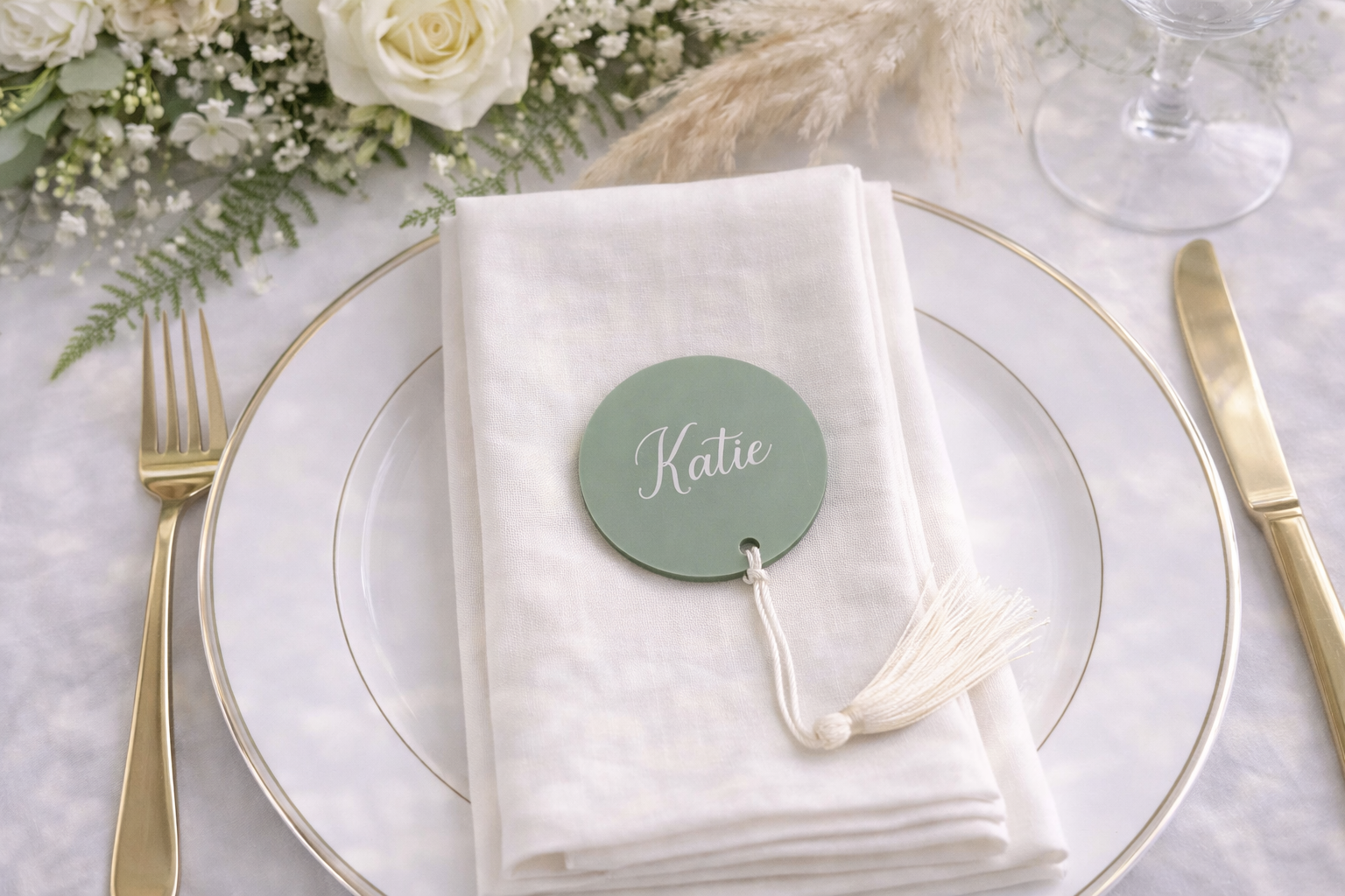 A table setting with a white napkin, a green circular name tag, and a gold fork and knife.