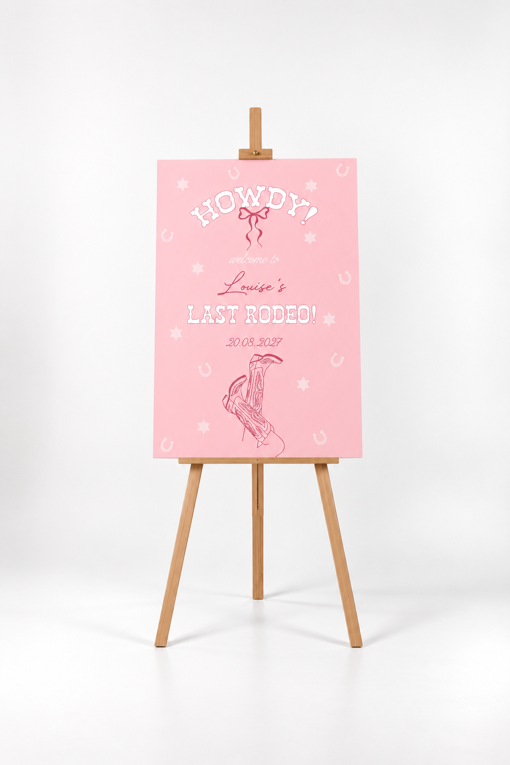 A pink poster with the text "HOWDY! Louisa's LAST RODEO! 30.03.2027" displayed on it, standing on a wooden easel.