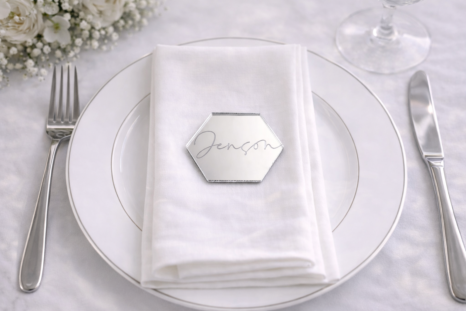 A place setting with a white napkin, silverware, and a small hexagonal name card with the name "Jenson" written on it.
