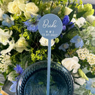 A blue wedding bouquet with white and blue flowers, and a blue circular sign with the text "Bride H & J 12.07.2027" placed in the center.