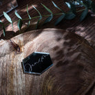 A wooden table with a black hexagonal placemat, a small plant, and a glass of water.