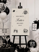 a black and white sign welcoming guests to a hen party, surrounded by various party decorations and items such as balloons, a cake, and a "TEAM Bride" sign.