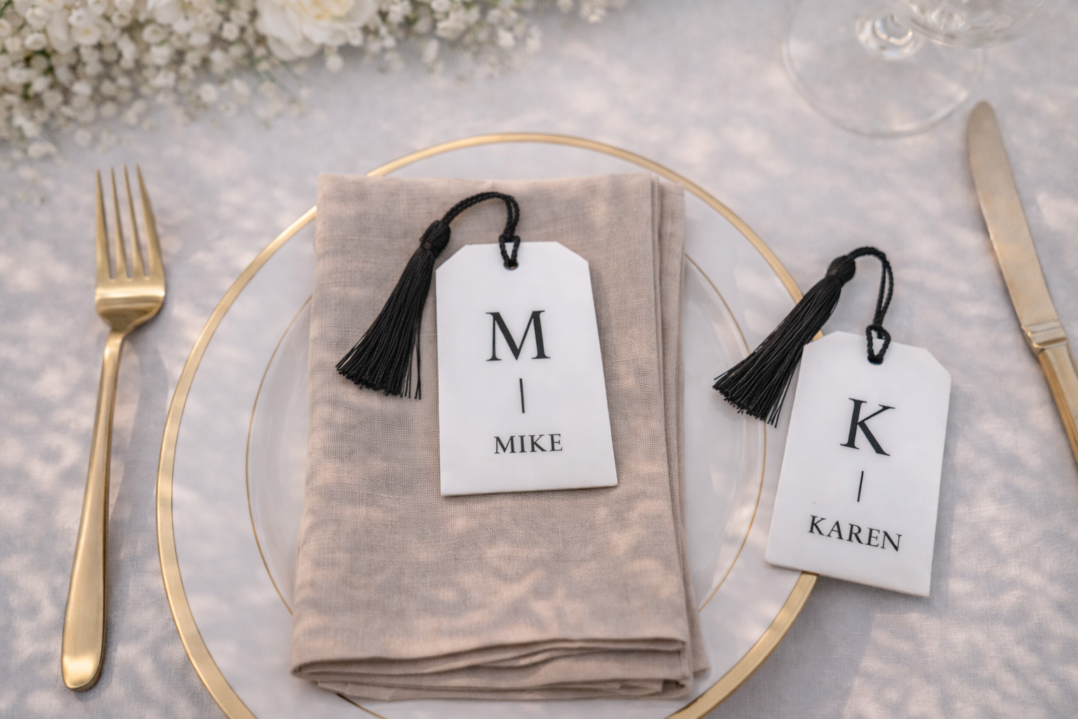 a table setting with a gold plate, a napkin, and two place cards with names on them. There is also a fork and a knife placed on the table.