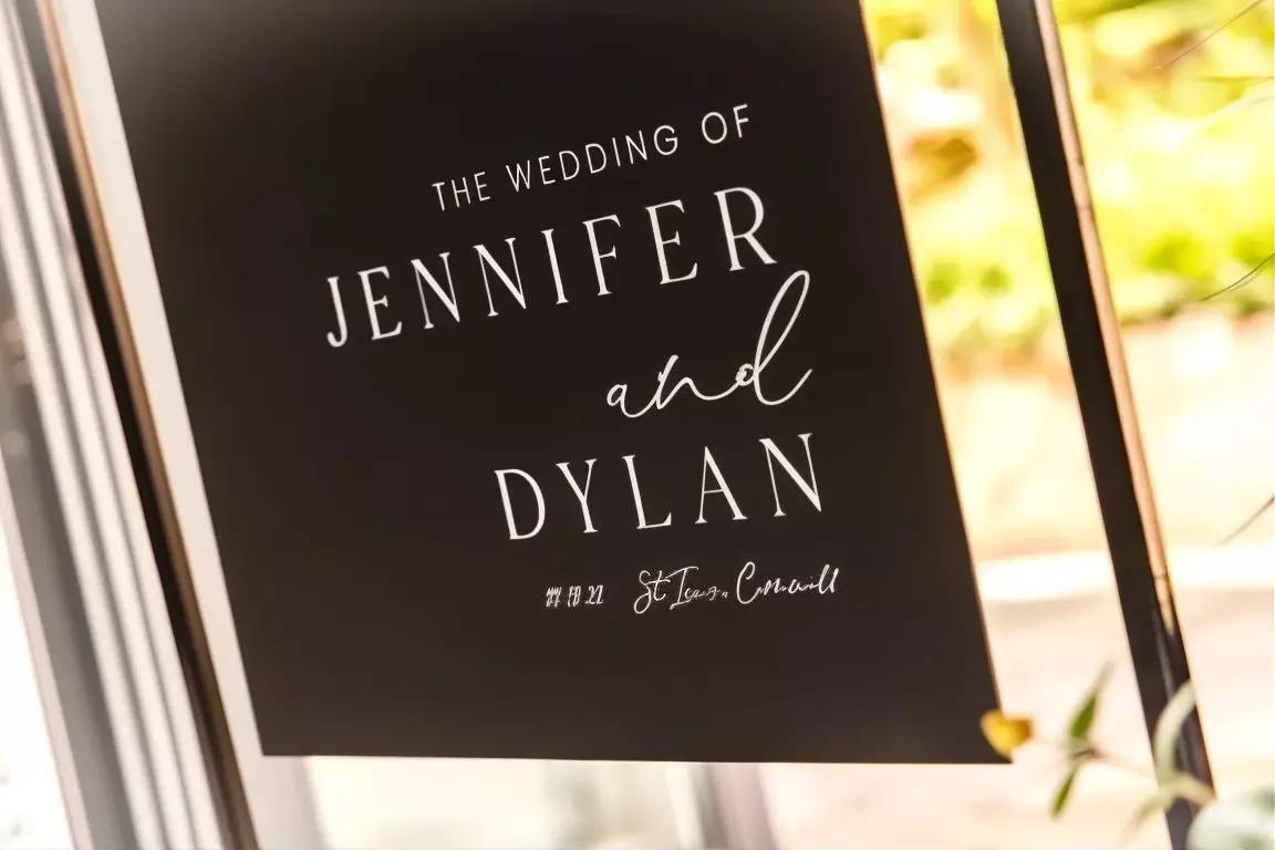 a black sign with white text that reads "The wedding of Jennifer and Dylan" and "St. Ian's Cornwell" written below it.