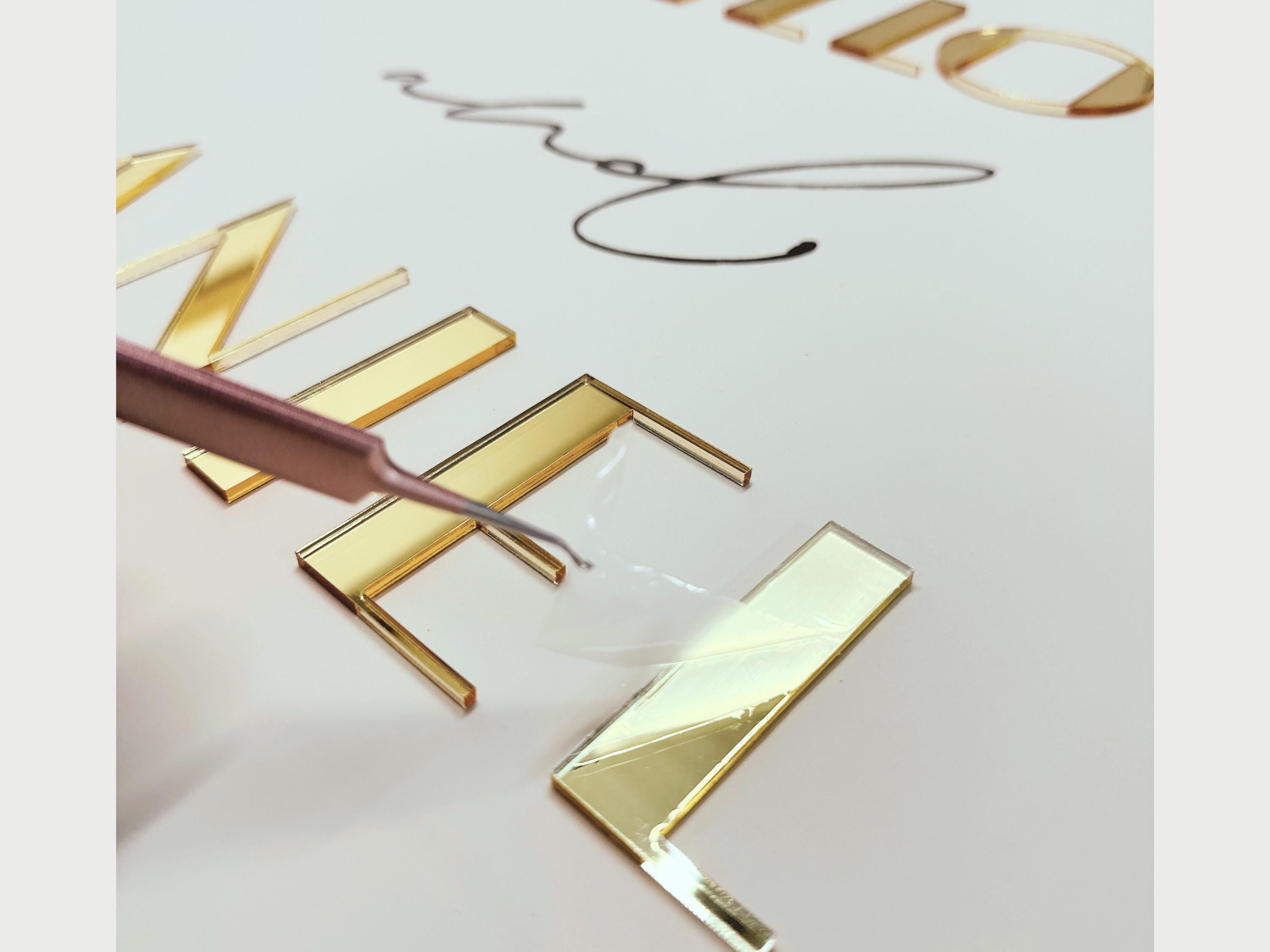 a close-up view of a person using a tool to cut or shape a piece of material, which appears to be a metallic or plastic object. The material has a golden-colored hue and is being modified with precision.