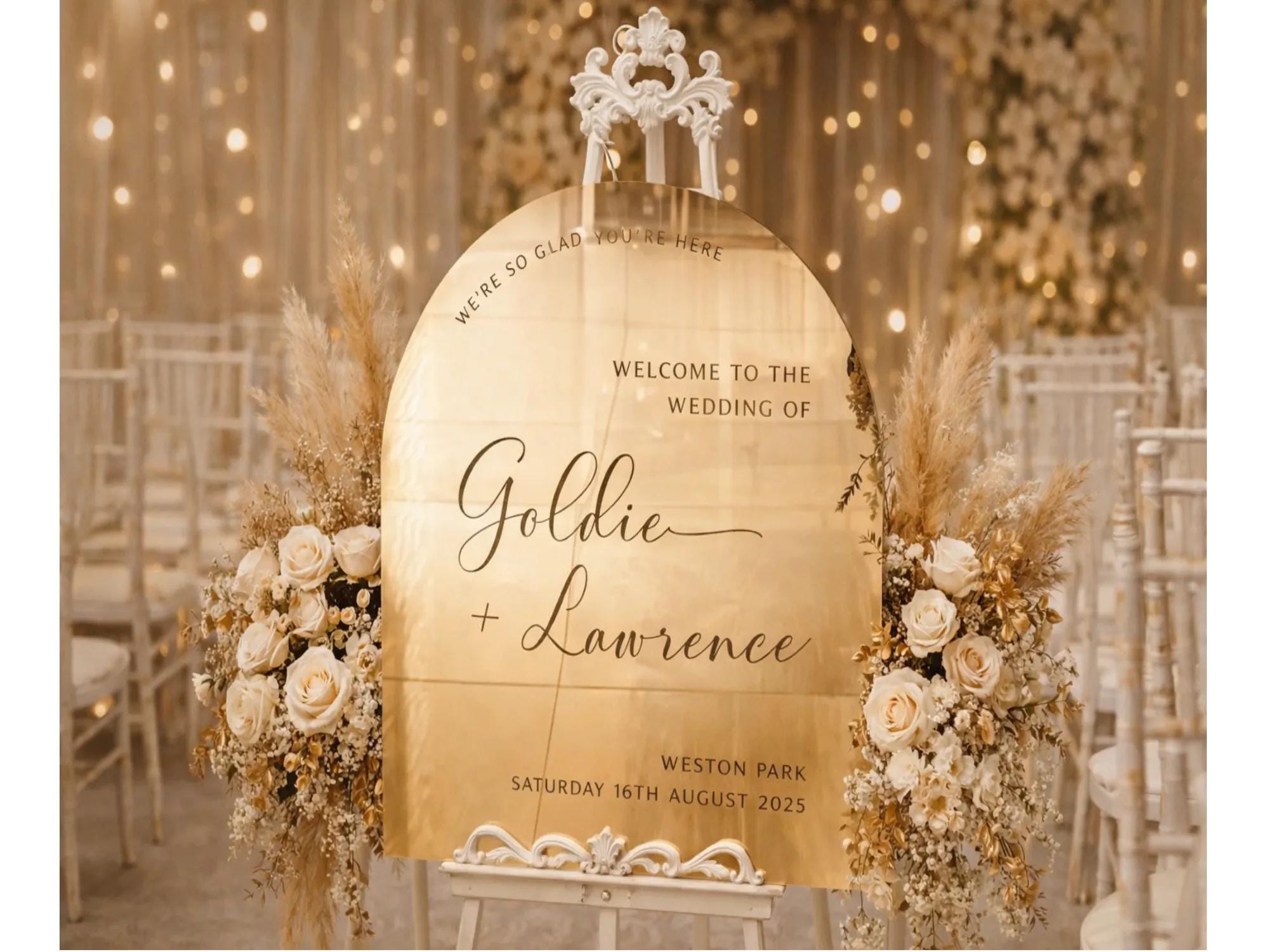 a wedding ceremony sign with the names of the couple, Goldie and Lawrence, and the date of their wedding. The sign is surrounded by floral arrangements and is placed in a setting with white chairs and a background of lights.