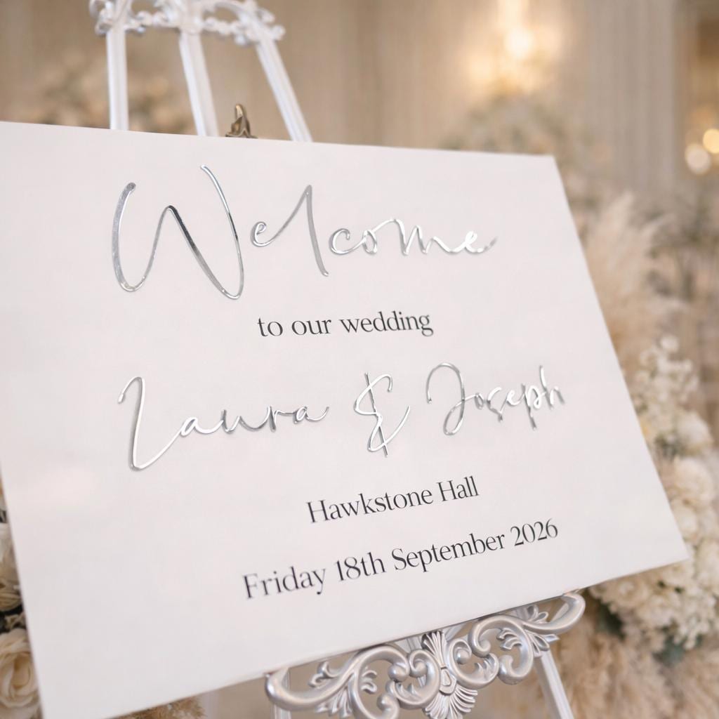 A white sign with elegant cursive text welcoming guests to a wedding.